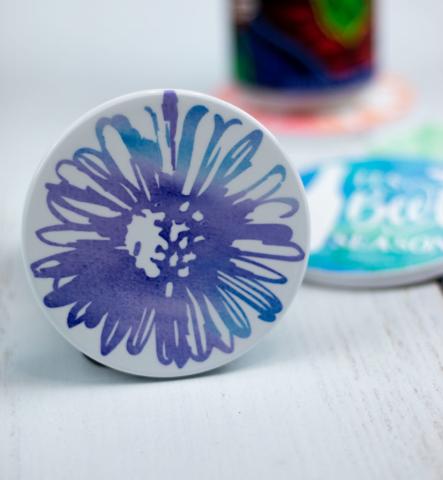 A ceramic coaster with a hand-drawn blue flower.