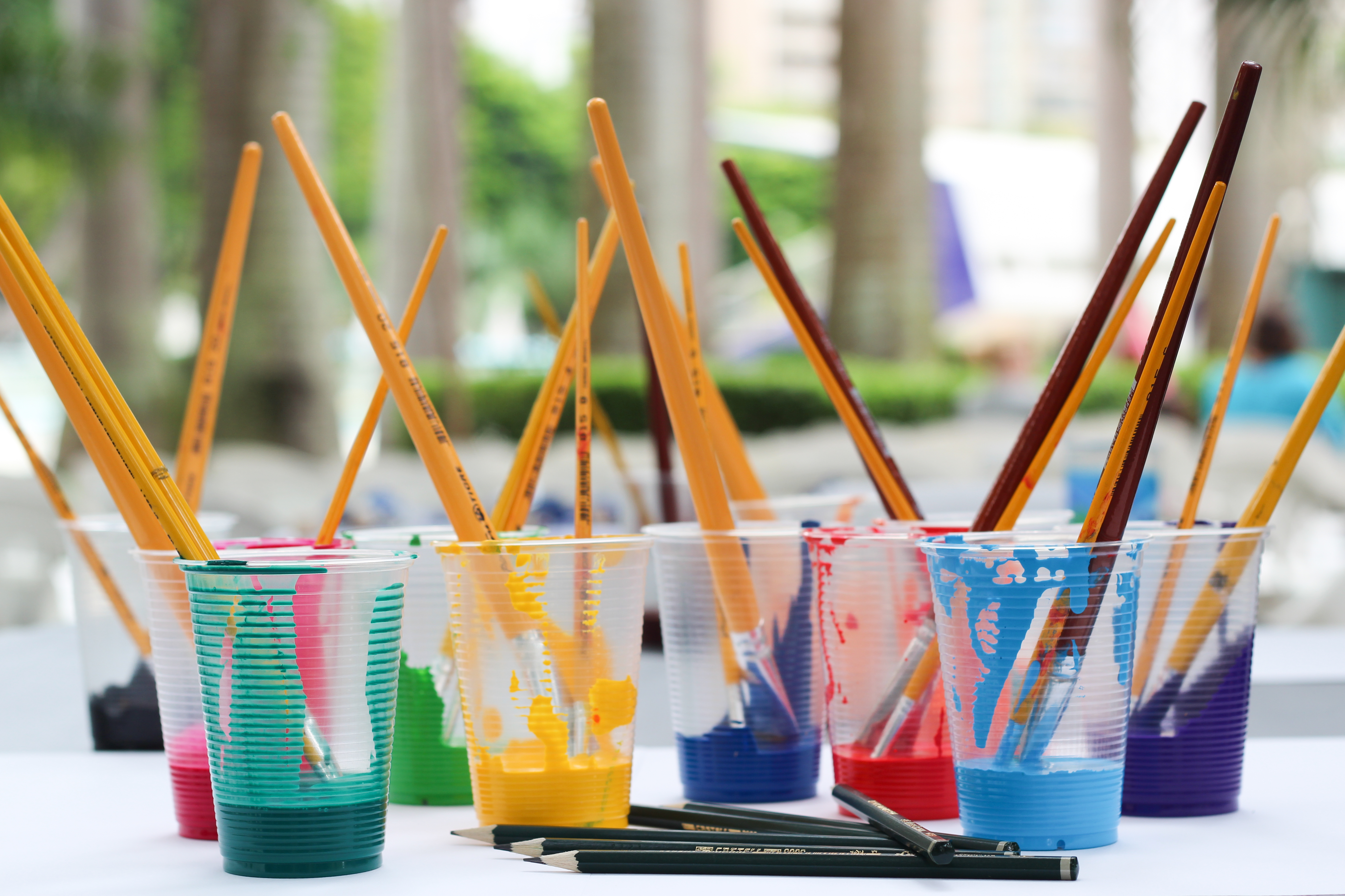 Paint brushes in cups of multi-colored paint.