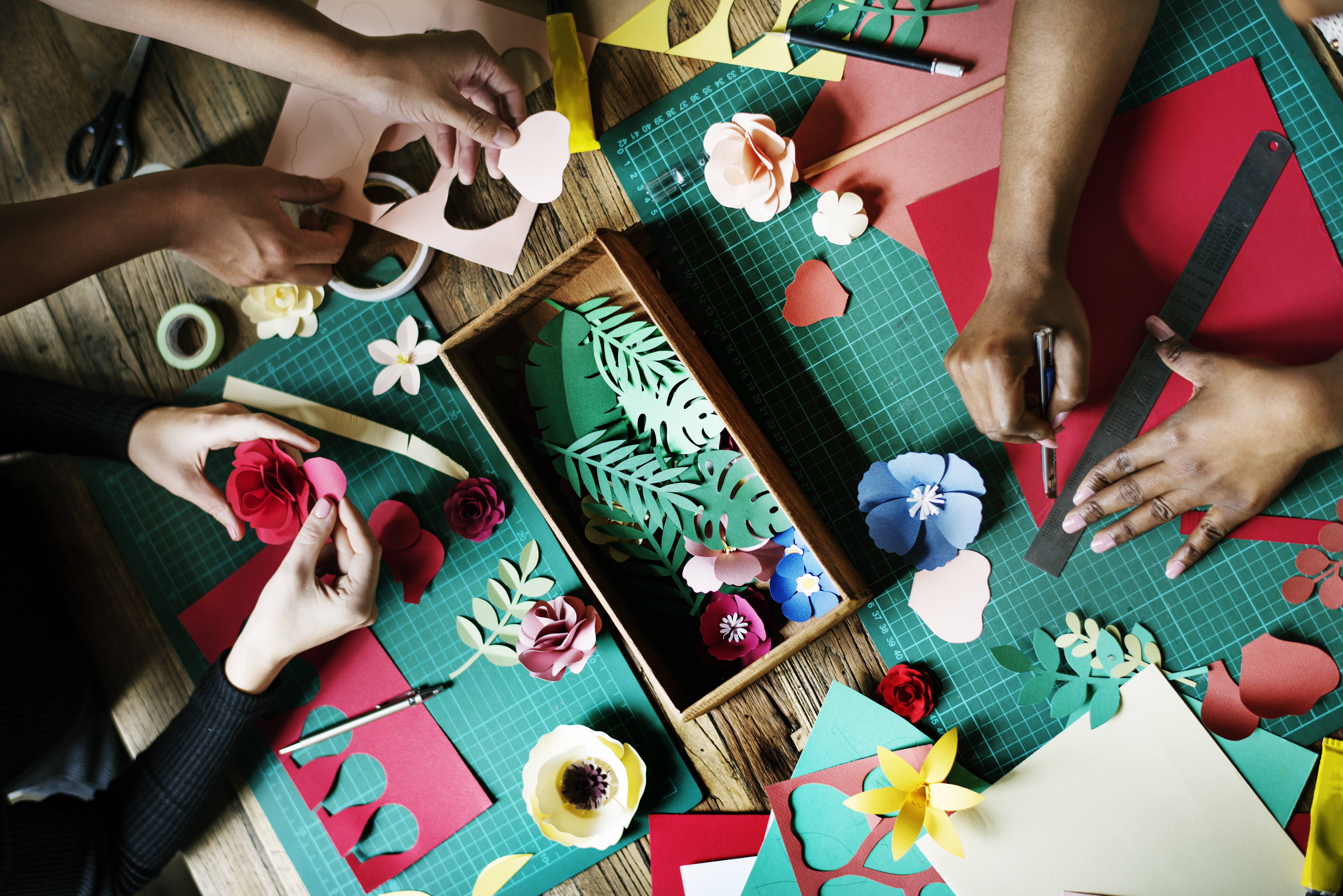 A photo of adult hands creating paper crafts at a table.
