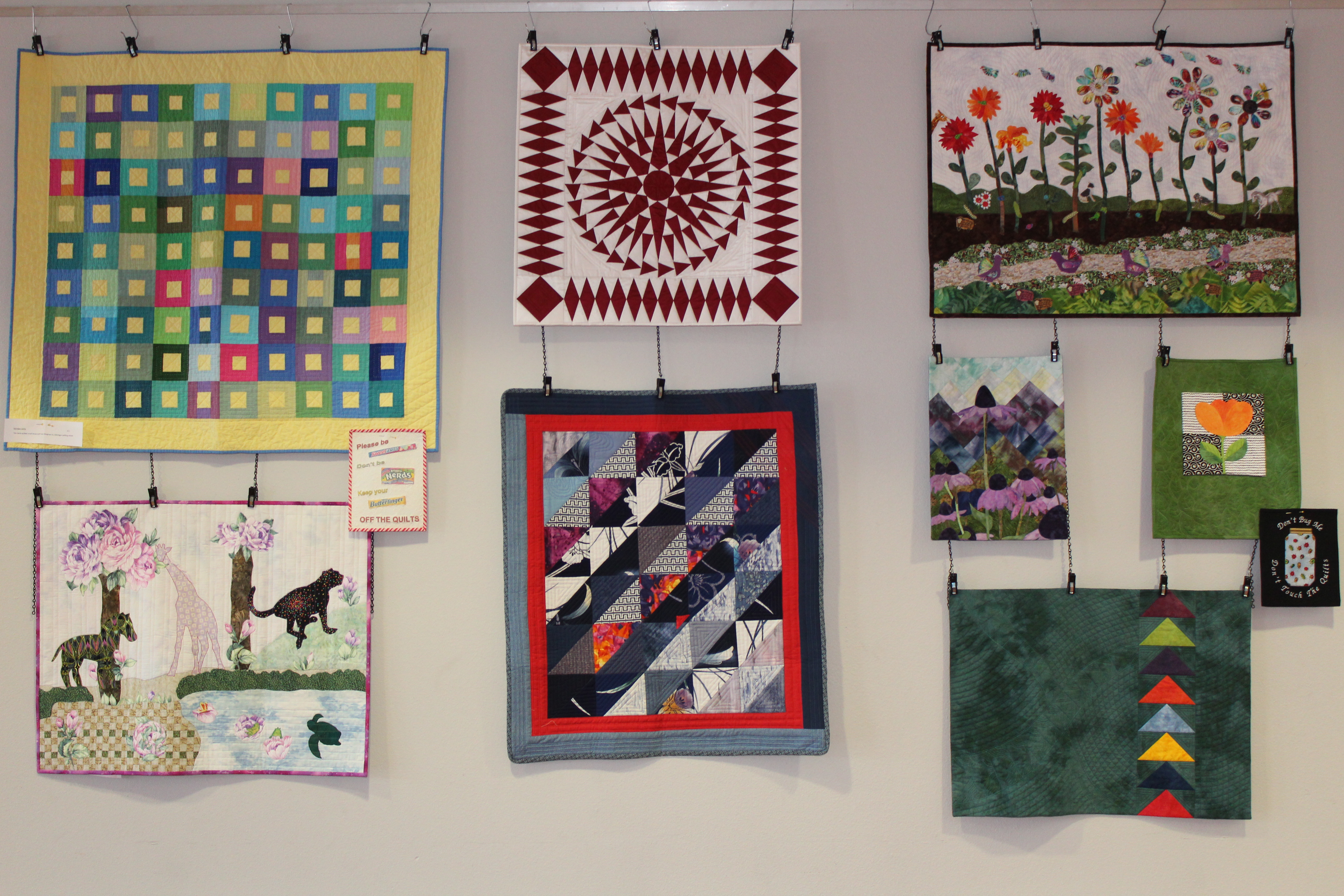 Eight Quilts hung on a wall. 
