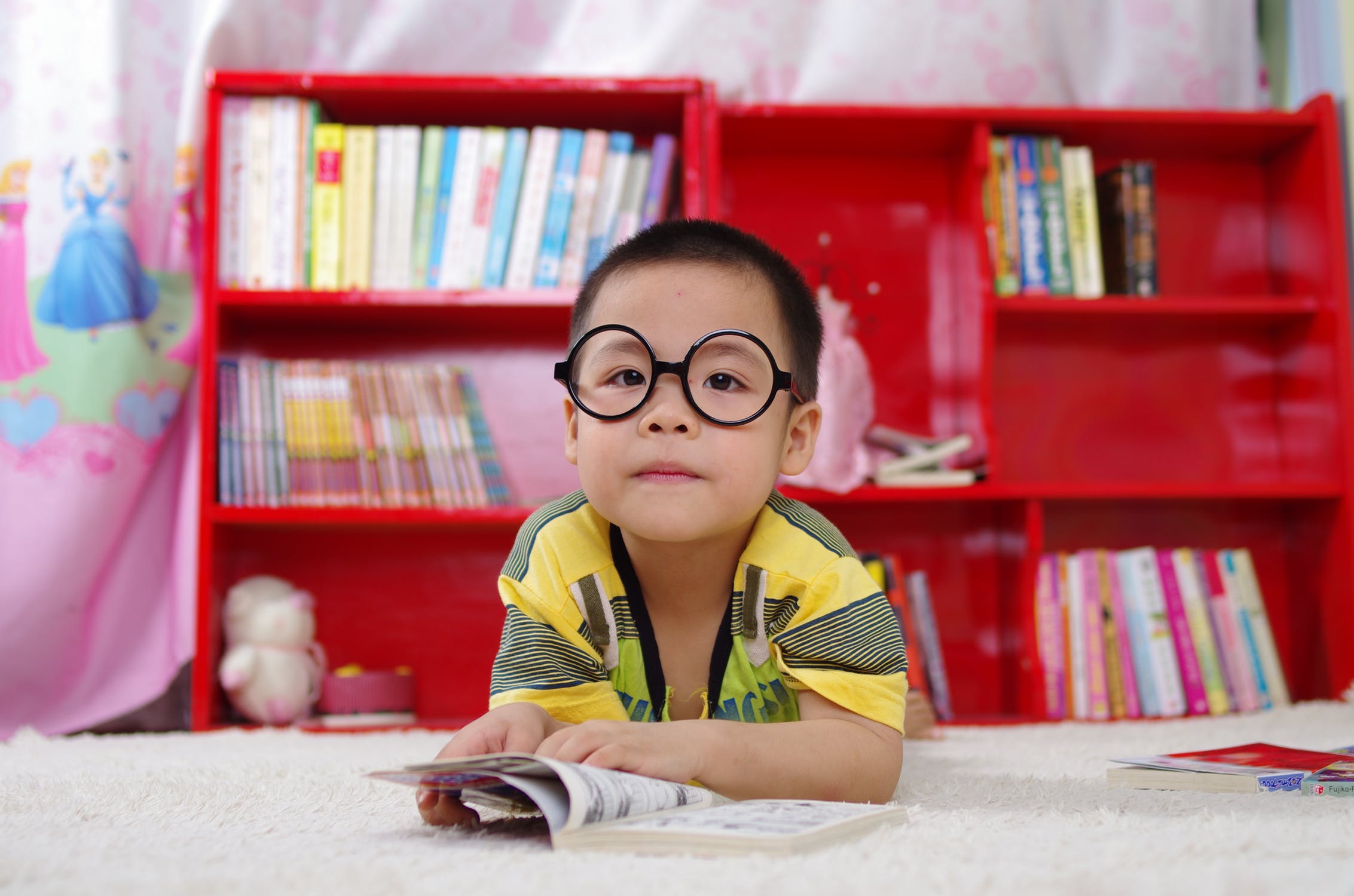 Boy reading a book with bookshelves behind him