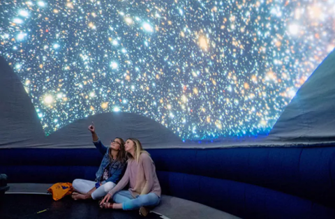 Two people sitting on the floor pointing up to a projection of the solar system.