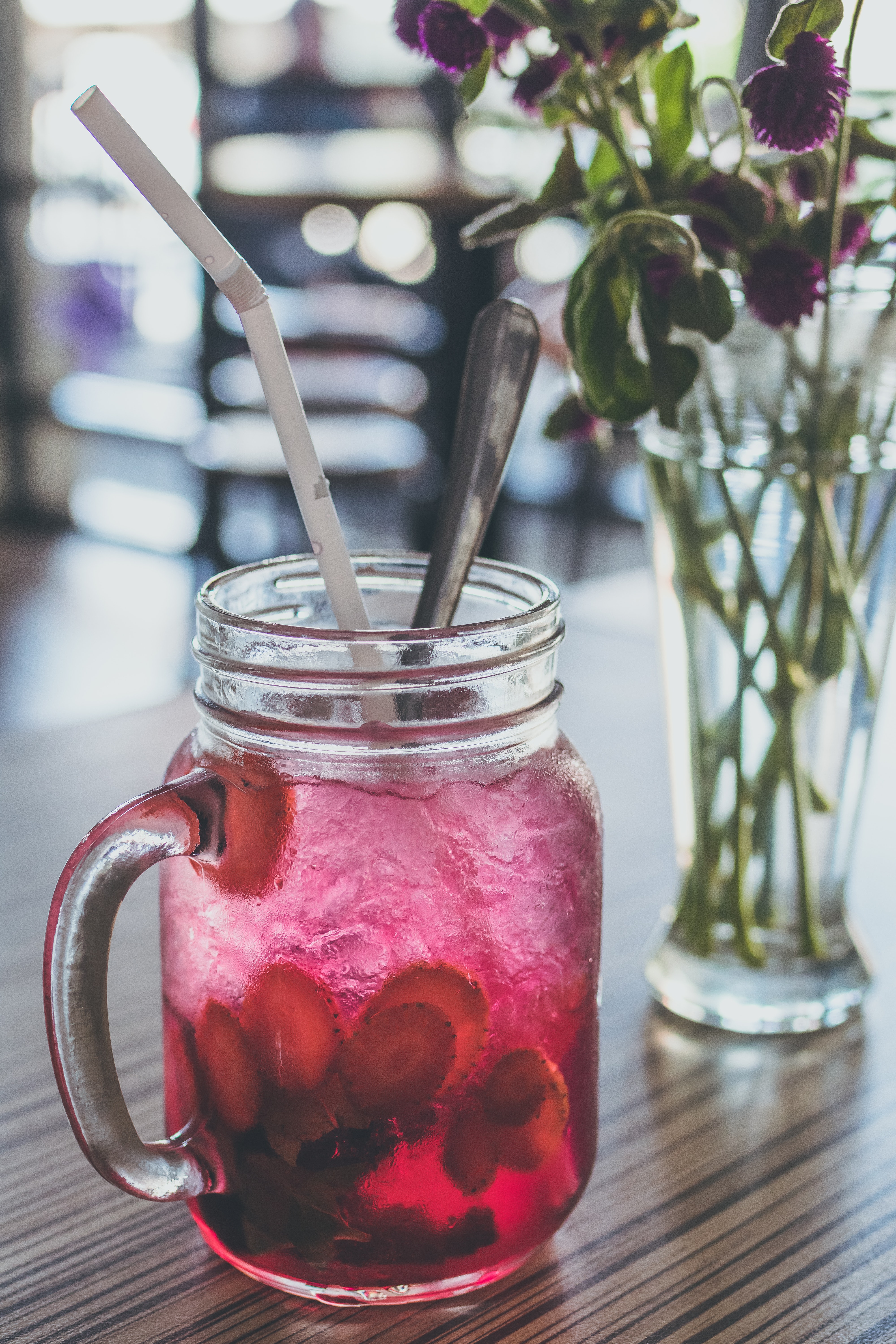 a mason jar sits on a table with pink liquid and bunches of berries in the bottom