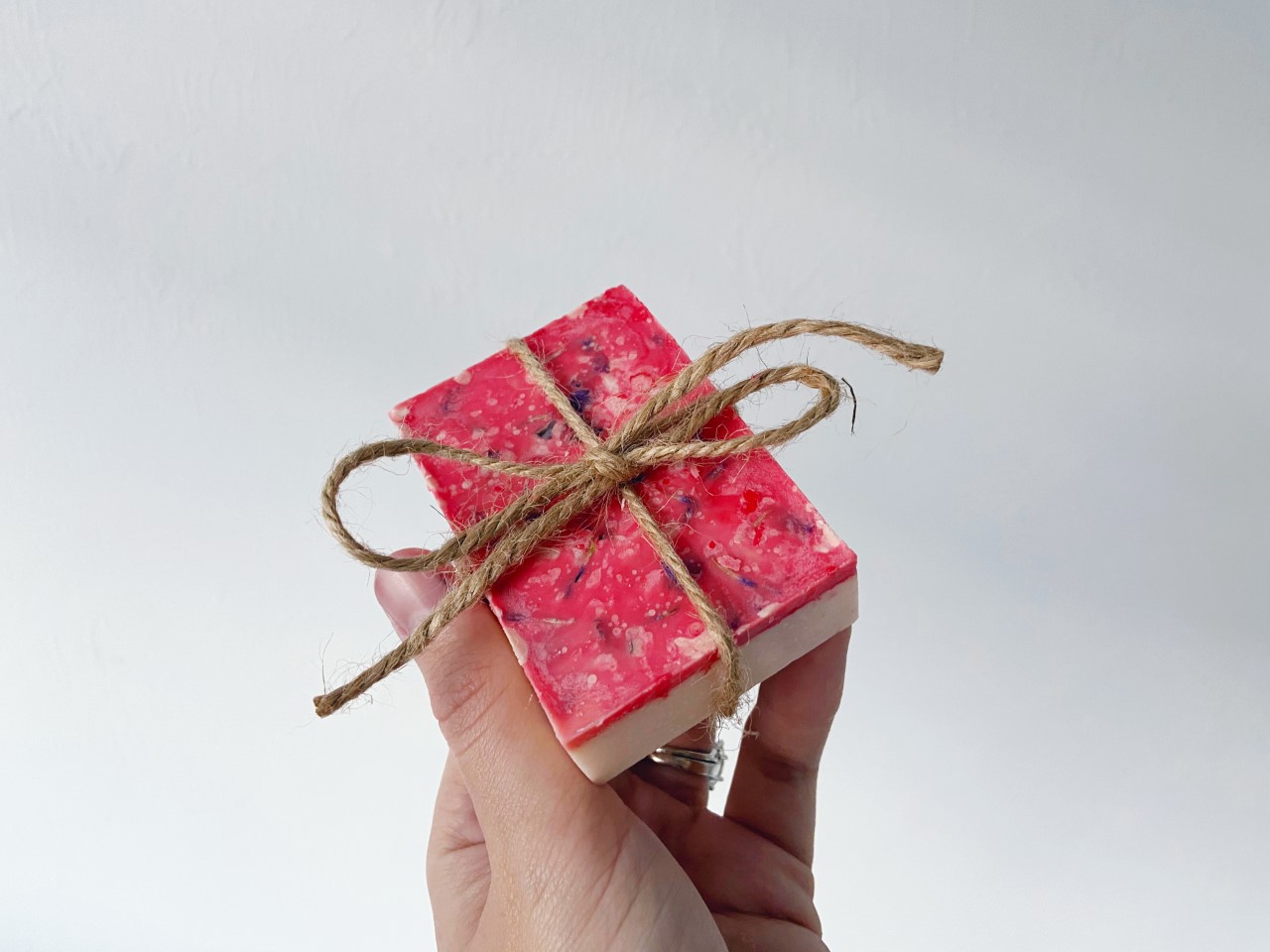 person holds up a bar of white soap with a flowery red top tied up with twine and a little bow