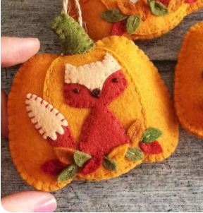 hand holds a felt pumpkin with a fox on it