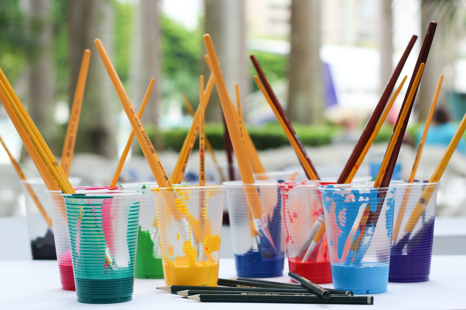 paintbrushes stand up in cups of colorful paint