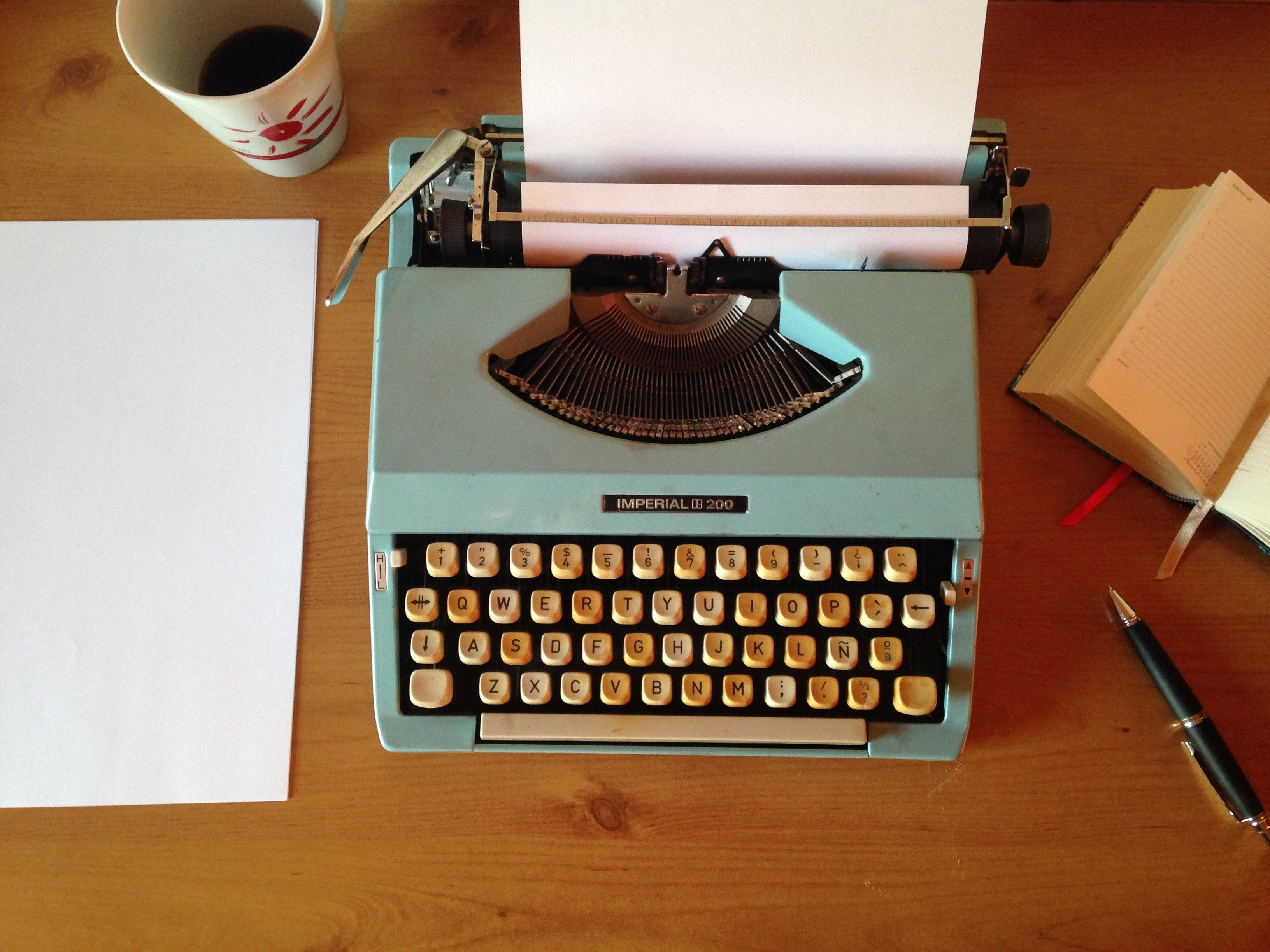 a typewriter sits on a wooden desk beside a cup of coffee