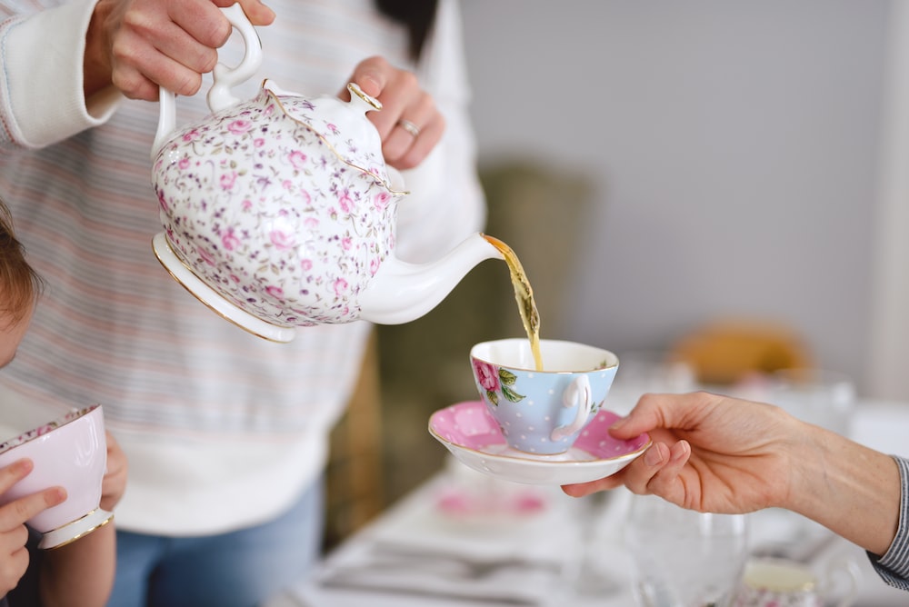 Person pouring tea into a cup from a decorative tea pot.