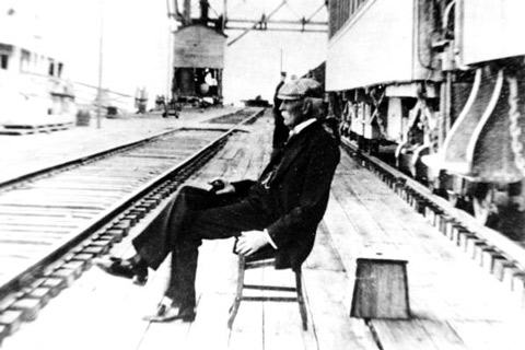 Black and white photo of a man (Henry Flagler) sitting in a chair at a train station.