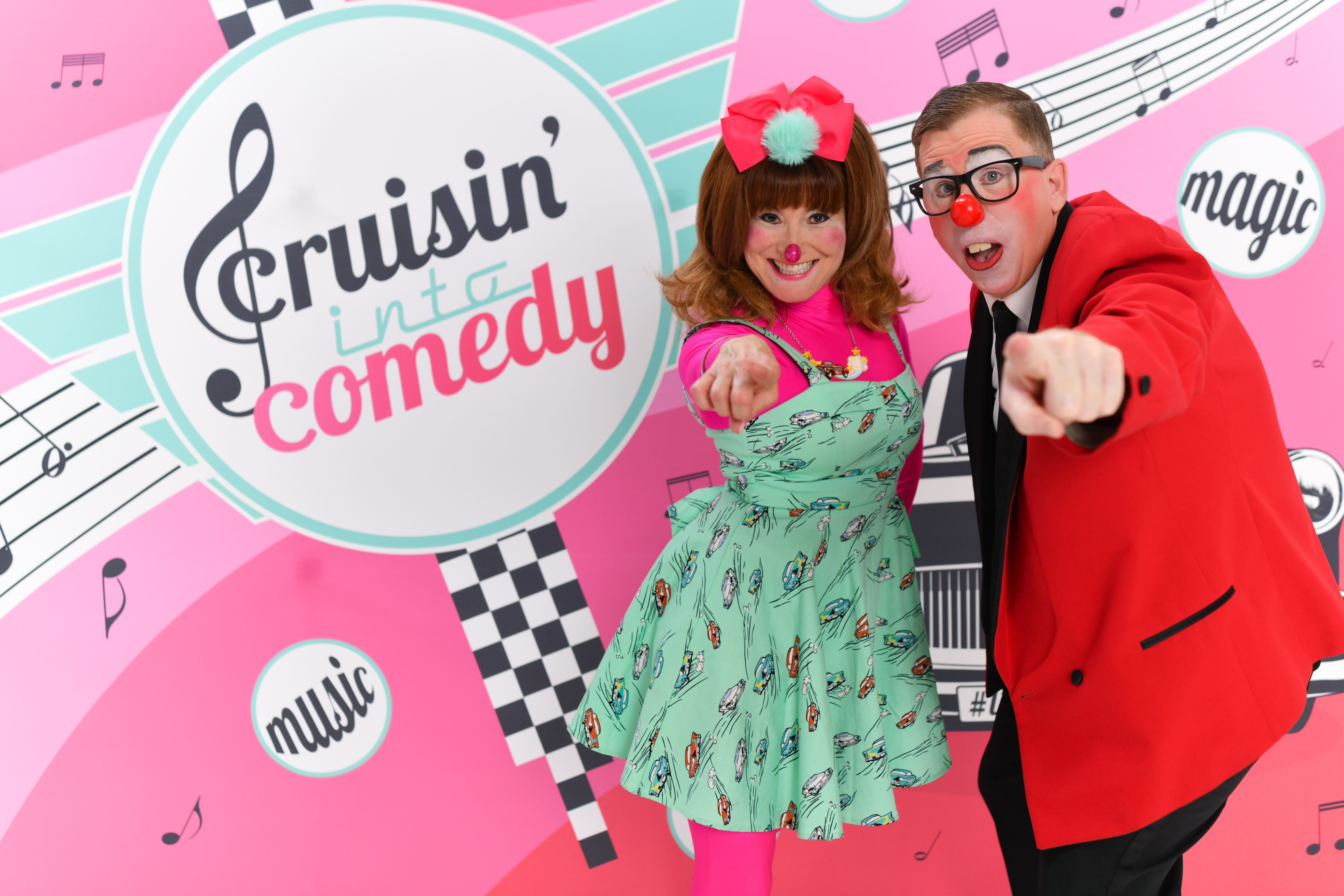 Woman and man dressed as clowns in front of a sign "Cruisin' Into Comedy".