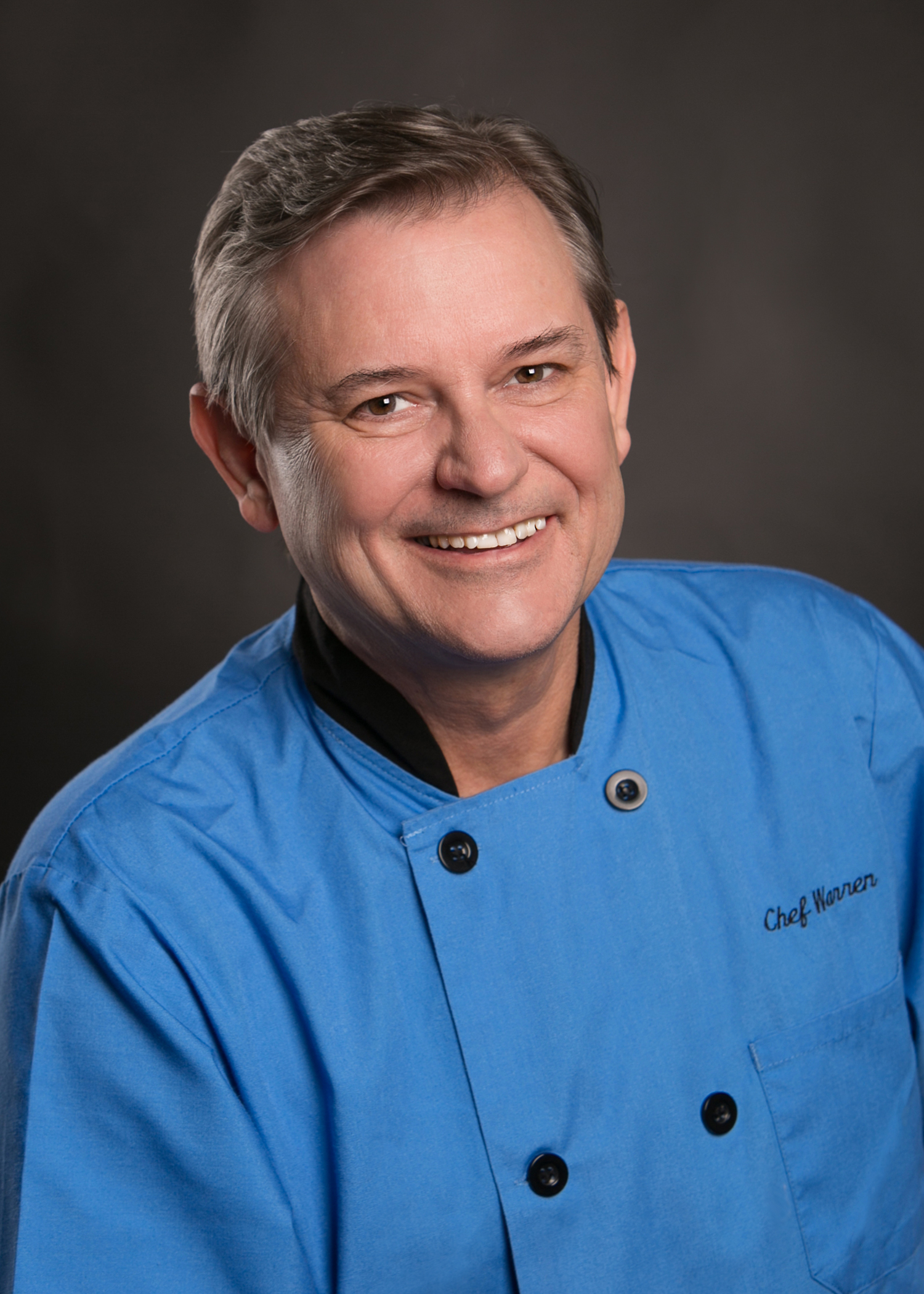 Chef Warren Caterson poses in a sky blue chef coat. 