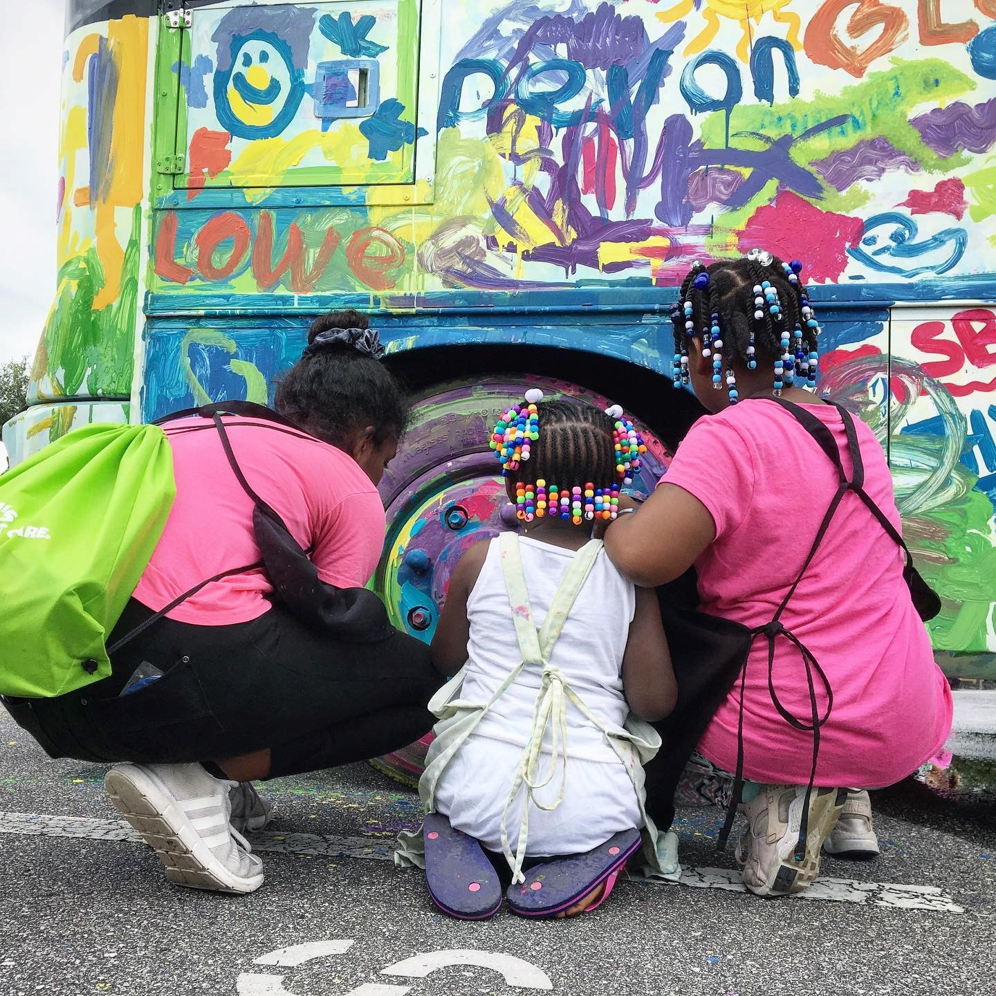 Kids painting a bus wheel.