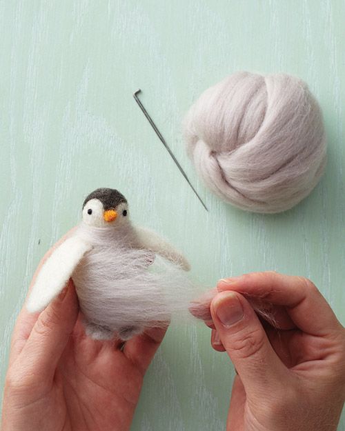 Ball of white felt material and crafting needle with two hands making a bird. 