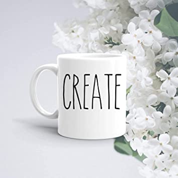 A white coffee mug with the word CREATE in black letters. White flowers are next to the mug.