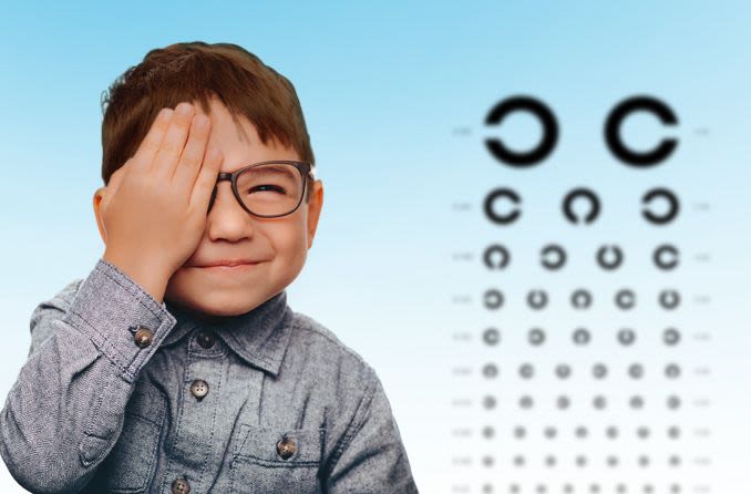 Little boy with his right hand over his left eye looking at an eye chart.