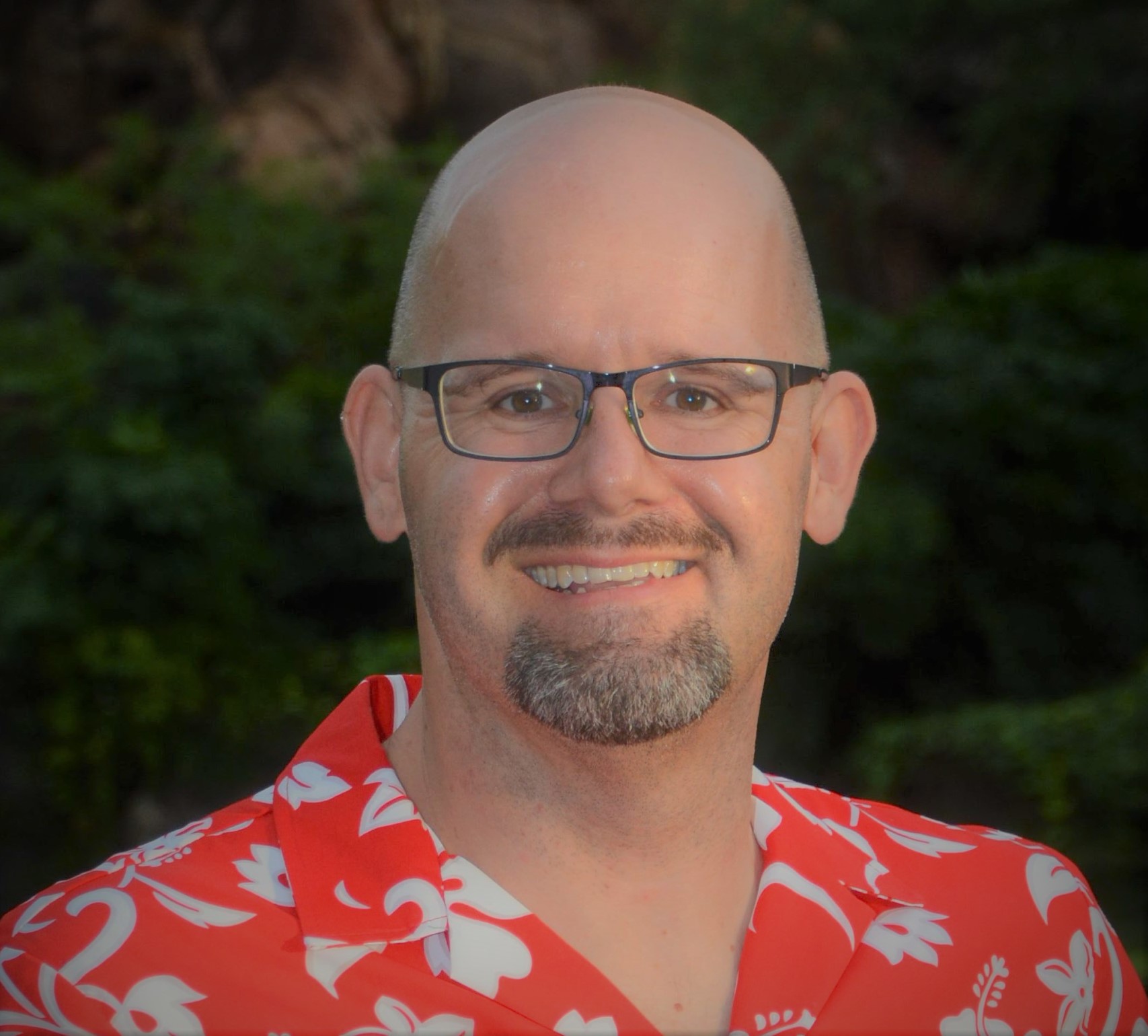 A headshot of author Rick Dakan wearing a red printed shirt.