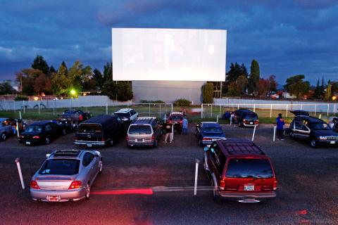 Outdoor movie screen with cars parked in front of it.
