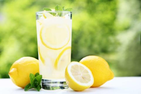 Tall glass of lemonade with fresh lemons next to the glass.