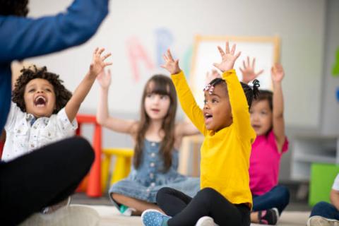 Children in colorful clothes seated and raising their hands.