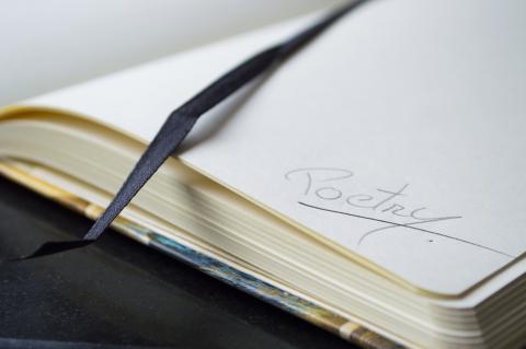 An open book with the word "poetry" handwritten on an otherwise blank page.