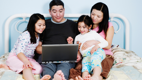 family of four on a bed using the computer together