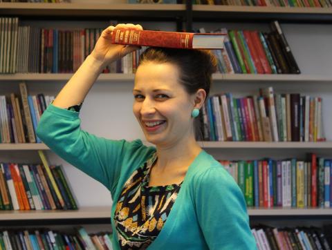 Smiling woman holding a book on top of her head.
