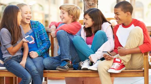 Group of five teens sitting on a bench laughing.