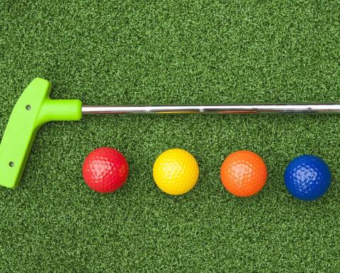 Mini golf putter and four multi-colored golf balls on a putting green.