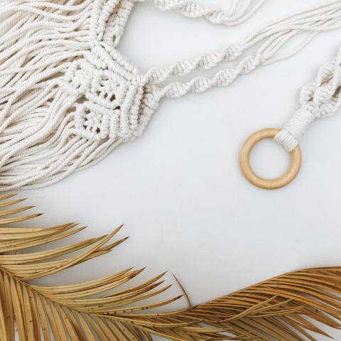 macrame laying on a white surface beside a tan palm frond