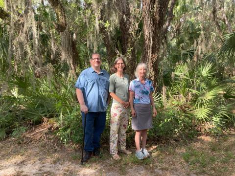 Ryan Van Cleave, Sylvia Whitman, and DIanne Ochiltree stand in a wooded Florida landscape.