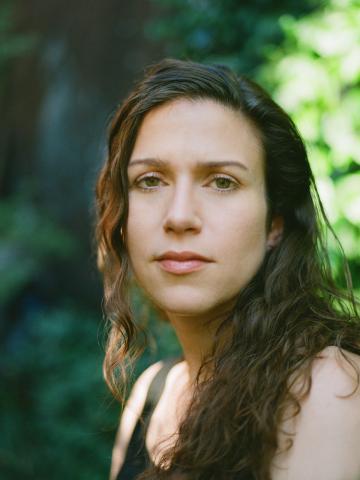 A headshot of author Emily Nemens with a green , leafy background.