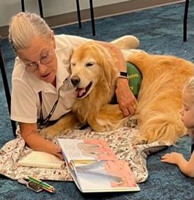 A picture of a therapy dog and her handler reading a book.