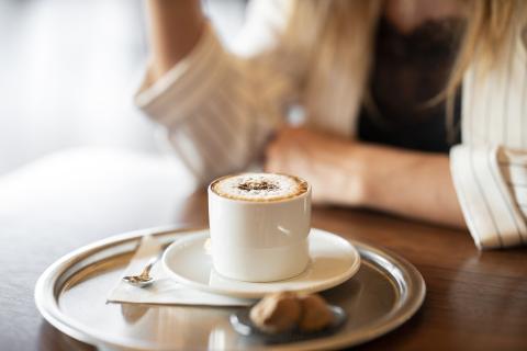 A cup of coffee sitting in front of a woman at a table.