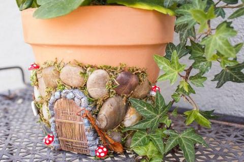A terracotta flower pot decorated with pebbles and straw to look like a small door on the side of the pot.