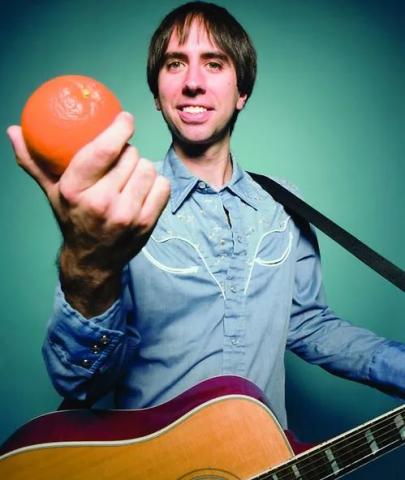 Photo of Chris Kahl holding an orange and a guitar.