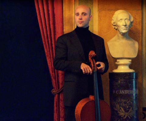 man with a cello standing next to a statue of Hans Christian Andersen