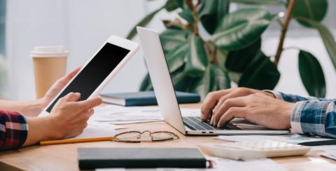 Picture of hands holding a tablet across from hands typing on a laptop.