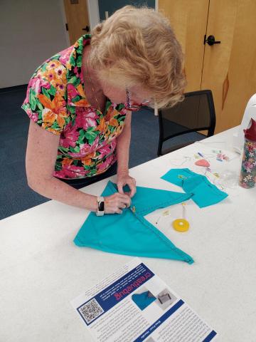 A lady measuring a blue fabric in the shape of a triangle.