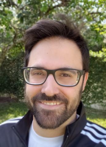 A headshot of writer and cartoonist Jarod Rosello wearing glasses outdoors.