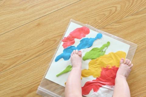 Paper with paint inside a resealable baggie with a pair of baby feet standing on it.