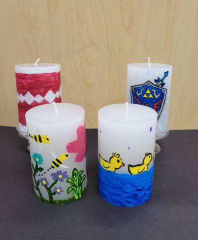 Four white pillar candles hand-painted with different designs