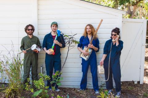 Four people wearing blue and green jumpsuits holding instruments made from recycled materials