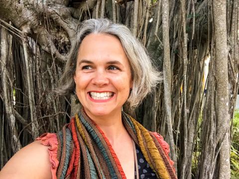 A smiling headshot of poet Laura Shoemaker infront of a banyan tree.