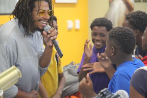Karim Manning holding a mic and smiling while teaching a group of kids.