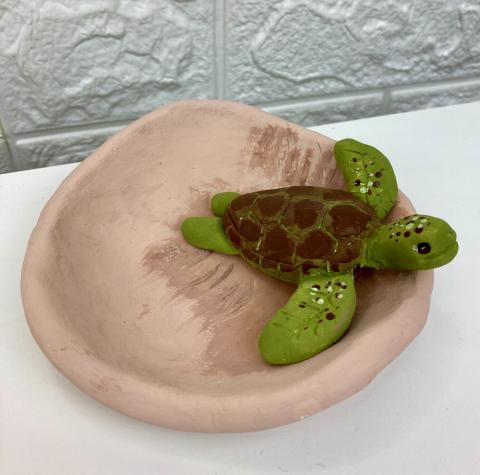 a green clay turtle in a brown clay bowl