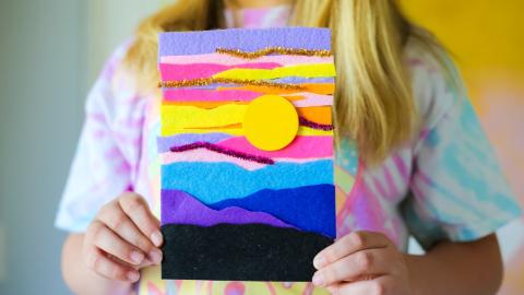 Person holding a felt collage picture of a sunset in various colors.