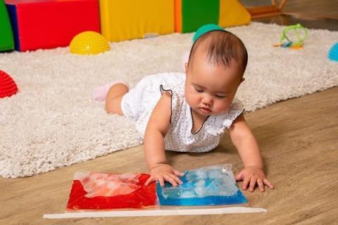 A baby on the floor playing with 2 bags full of colored water