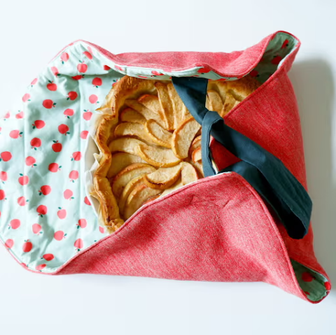 An apple pie sitting in a pie carrier made with red and blue fabric. 