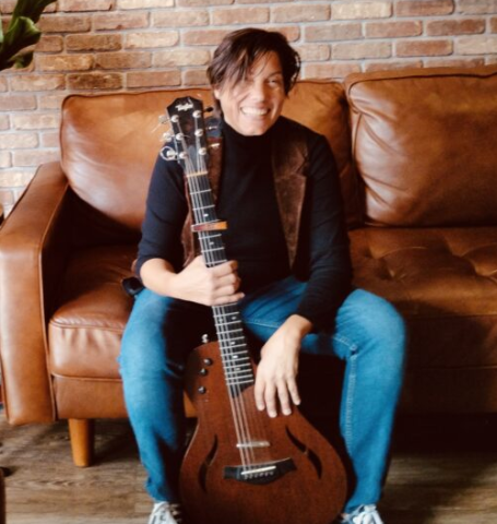 Musician Sandi Grecco sitting in a couch holding a guitar