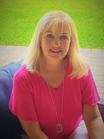 A picture of a smiling women with blonde hair and a pink shirt.